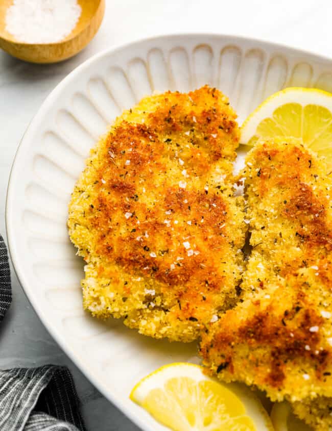 fried chicken breasts on a white plate with lemon wedges.