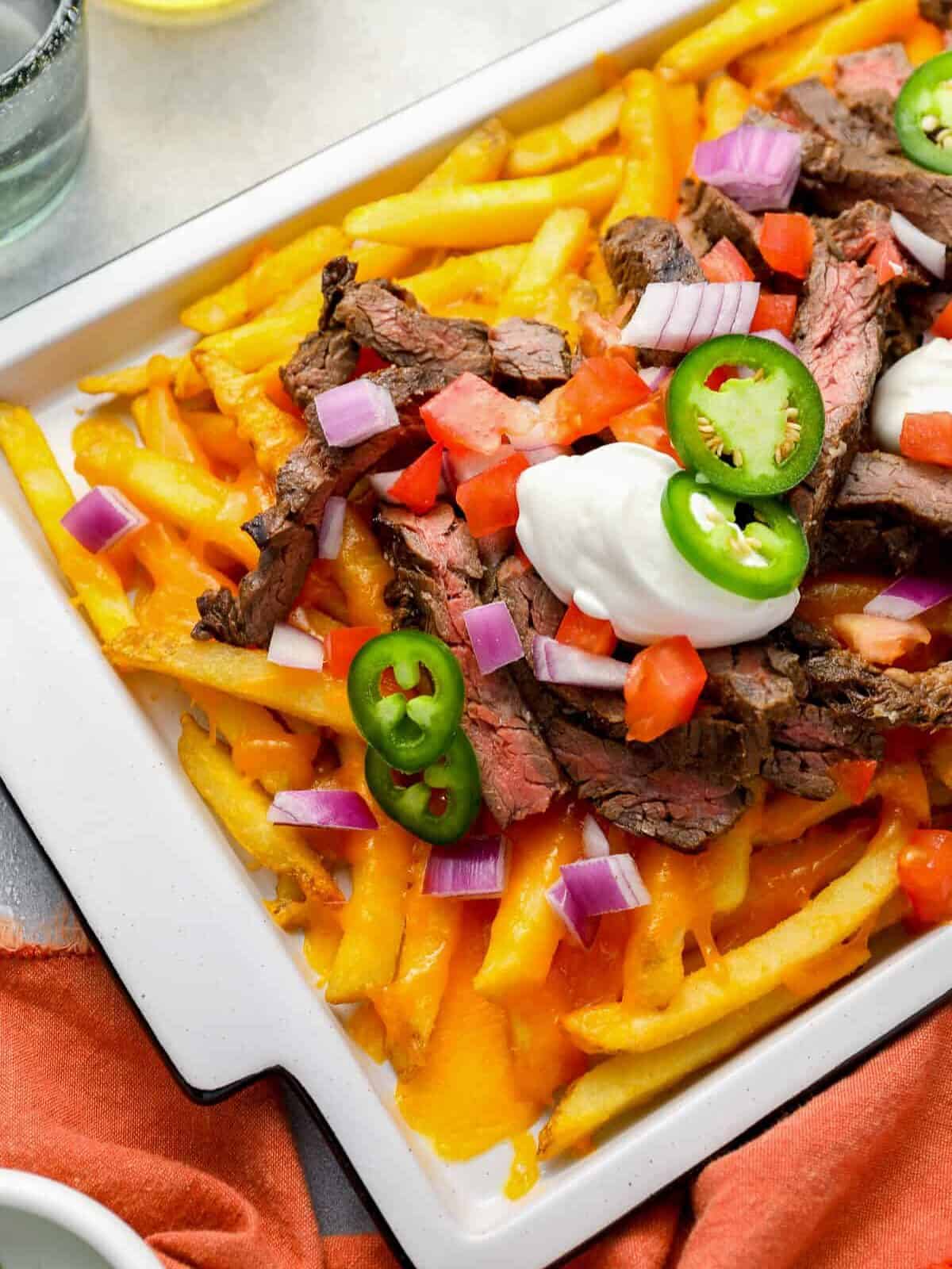 partial overhead view of fries topped with cheese, carne asana steak, jalapeños, and sour cream