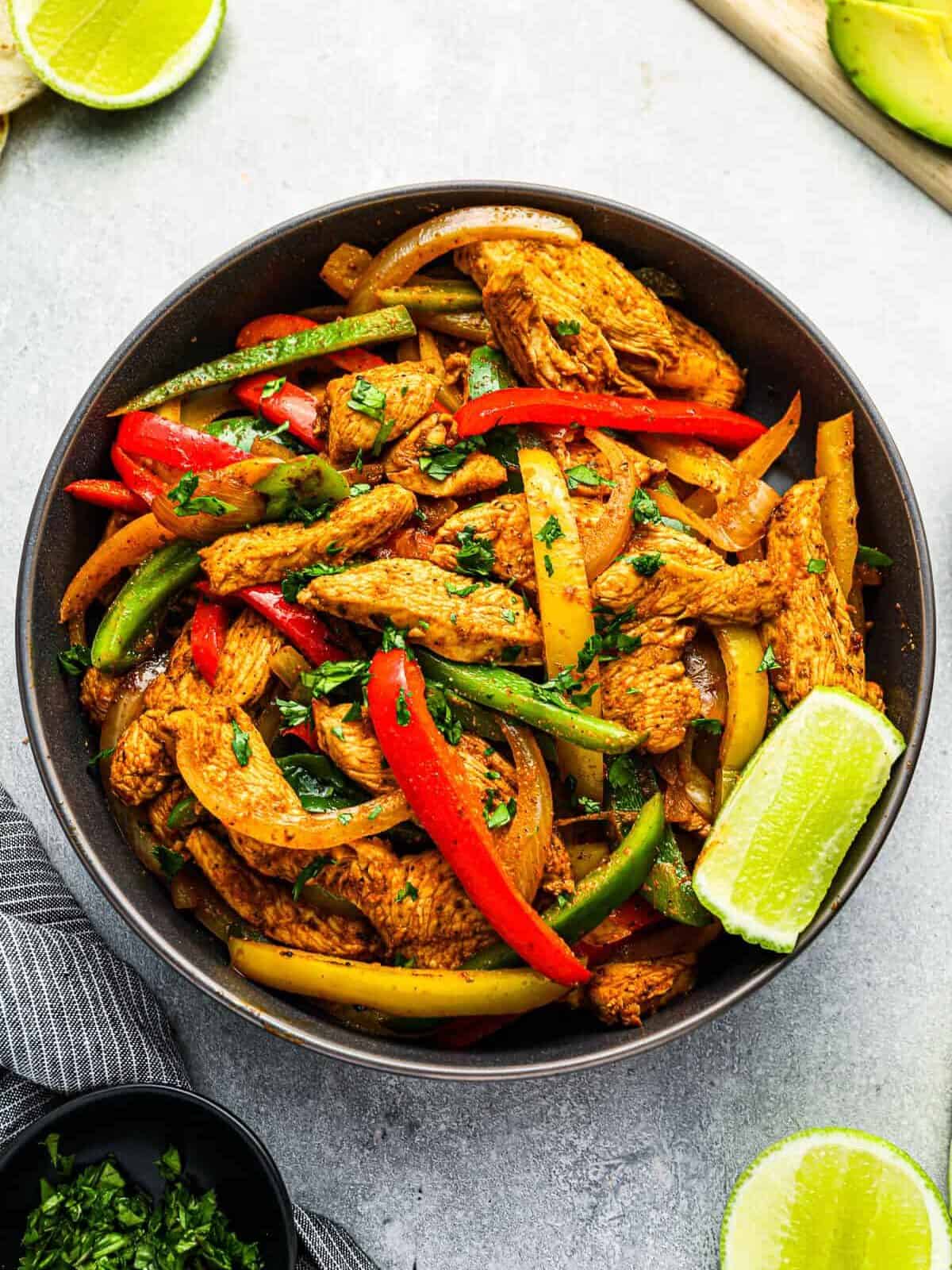 overhead view of chicken fajitas filling in a black bowl with a lime wedge.