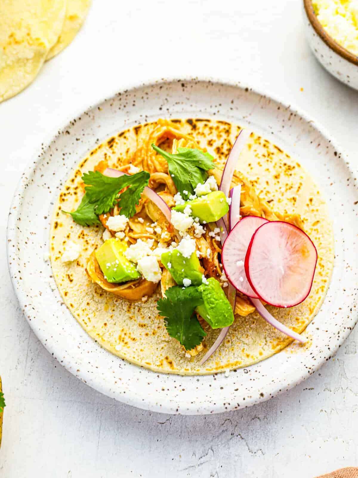 three-quarters view of chicken tinga tacos laid flat on a speckled white plate.