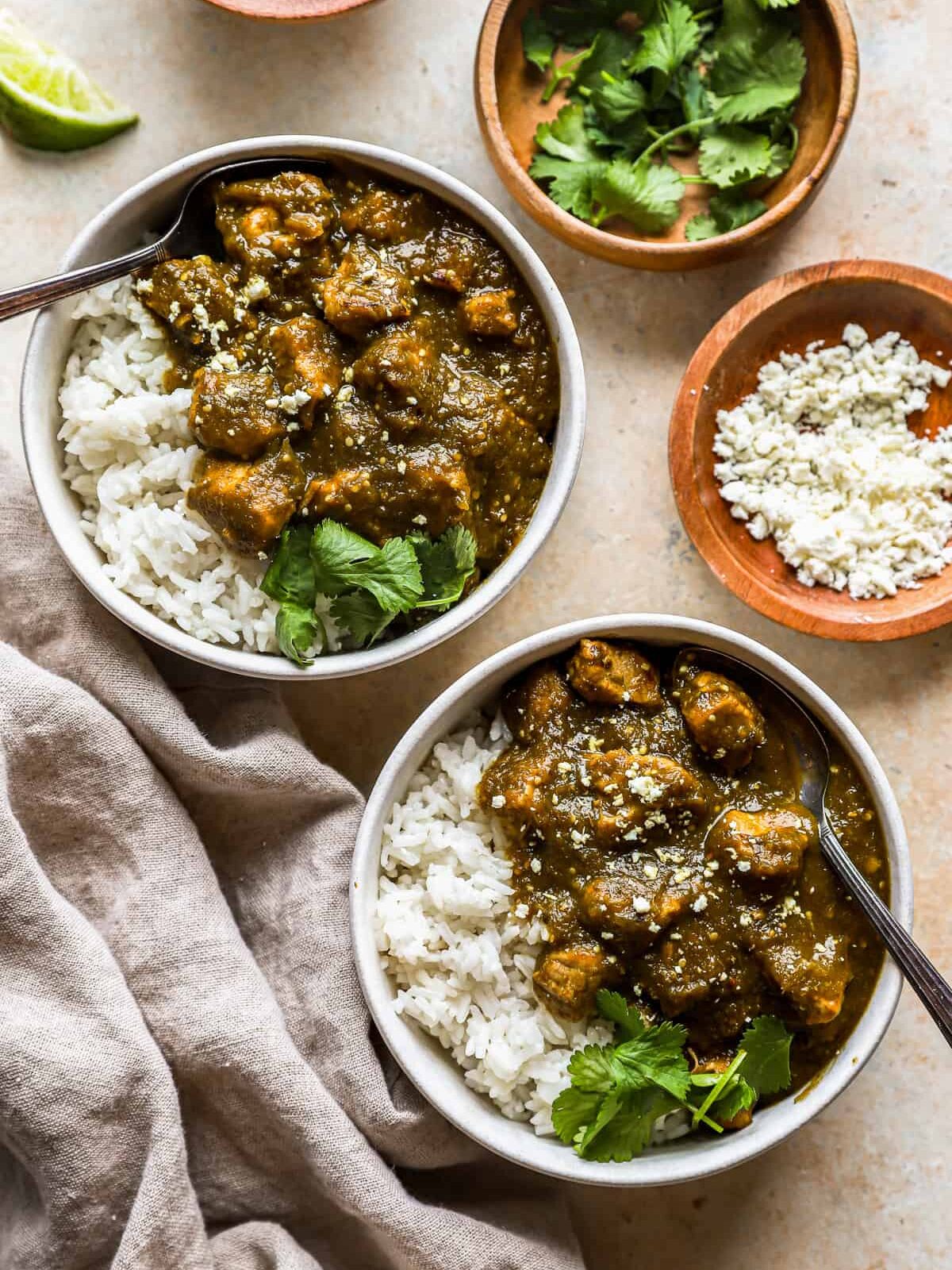 overhead view of 2 bowls of green chili with forks and white rice.