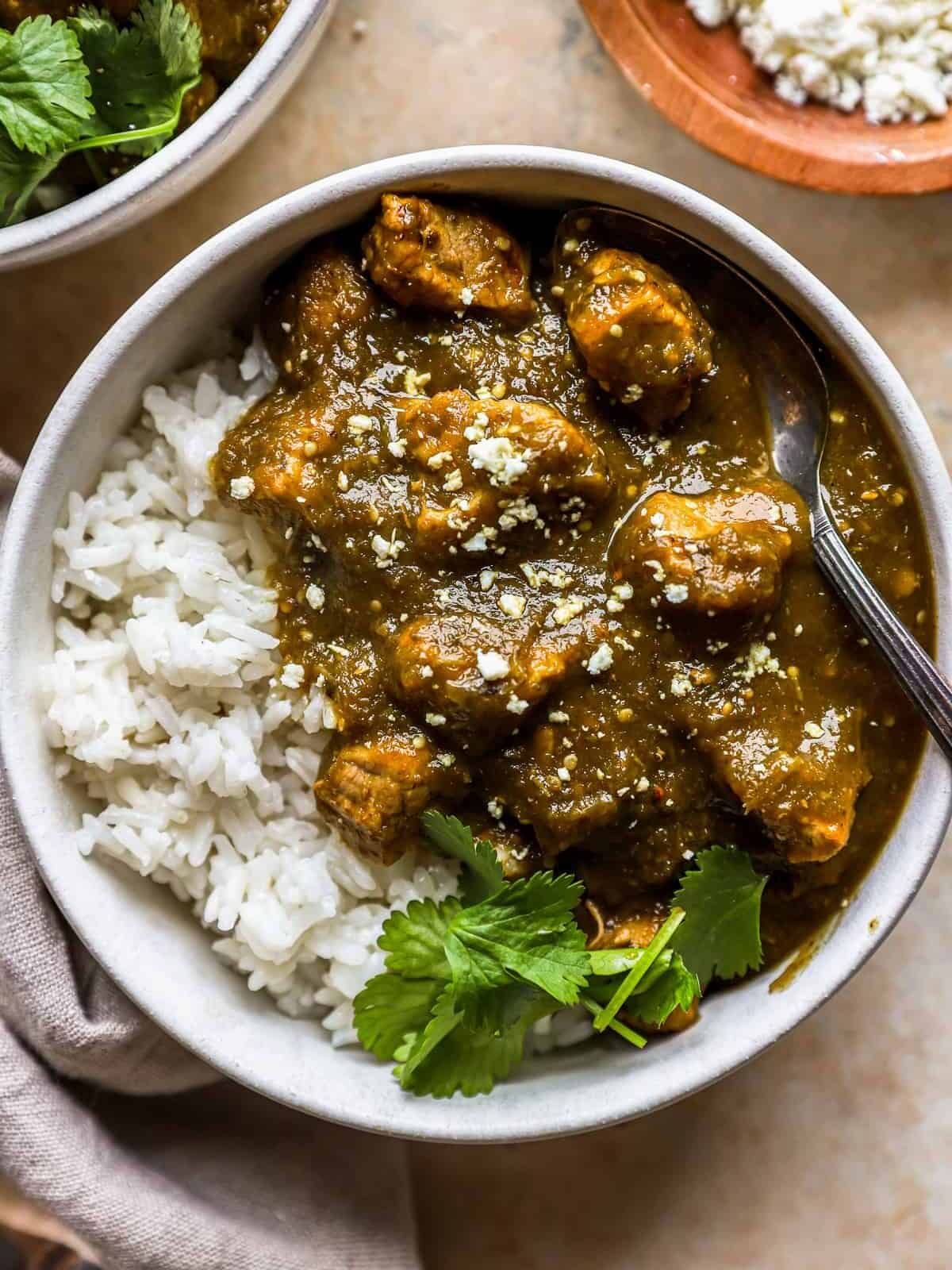 overhead view of a serving of Chile verde (green chili) in a white bowl with white rice, cilantro, and a fork.