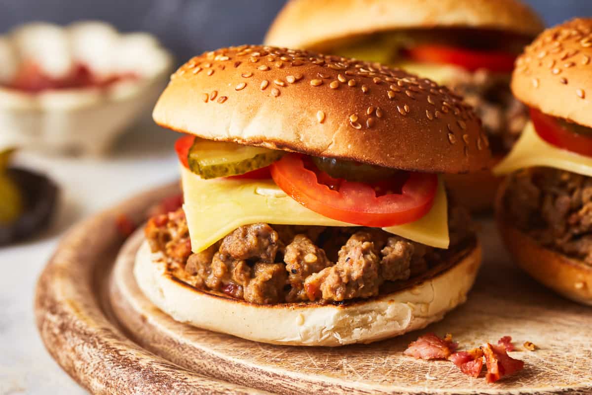 close up side view of a cheeseburger sloppy joe on a round wooden cutting board.