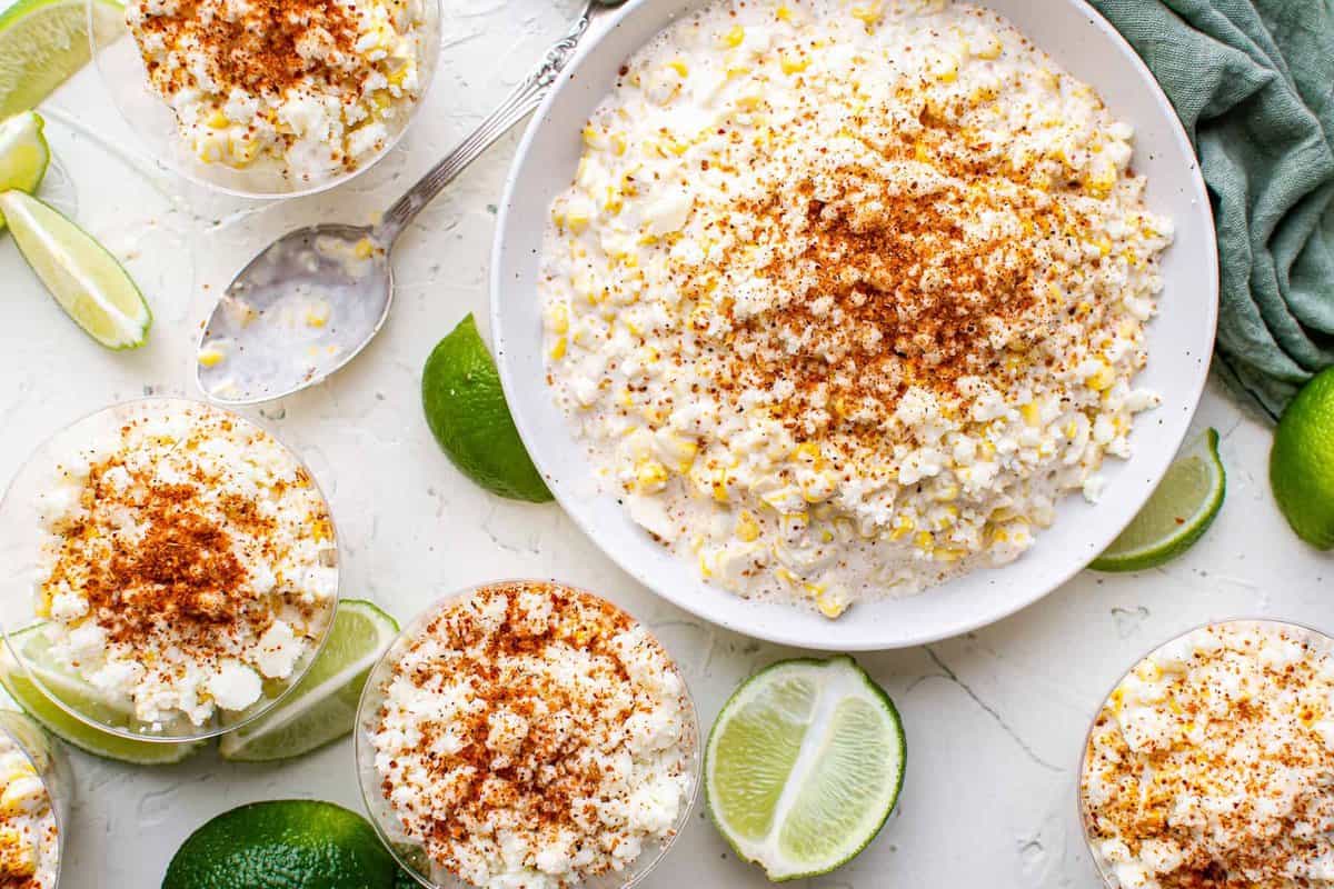 overhead view of a serving bowl full of esquites, surrounded by small cups full of the Mexican street corn salad