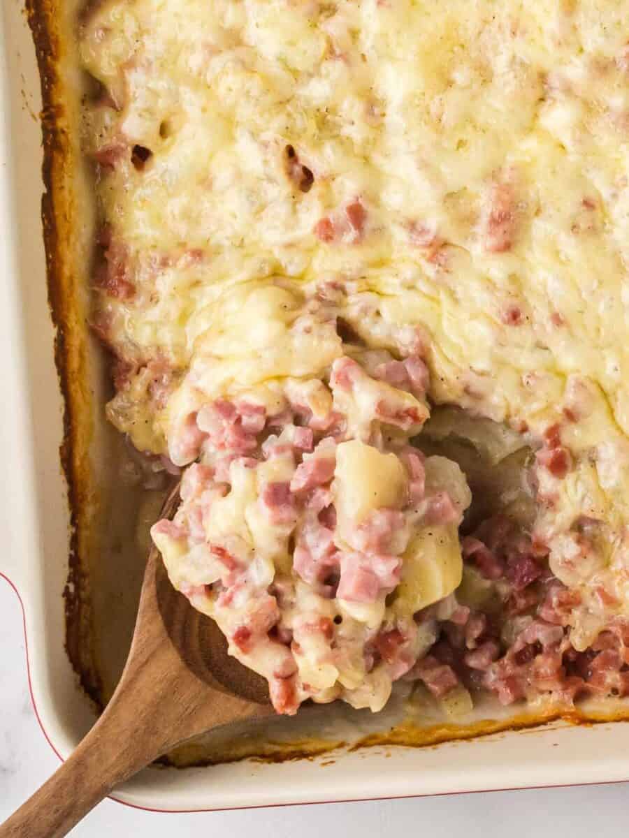 overhead image of ham and potato casserole with a wood spoon with a serving scooped out