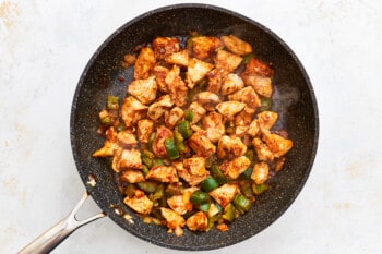 chicken, bell peppers, and onions cooking in a skillet