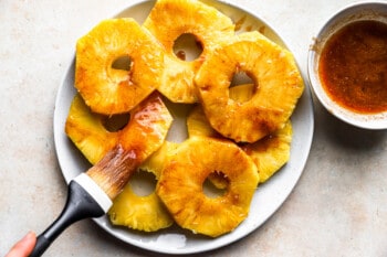 a hand brushing glaze onto pineapple slices.