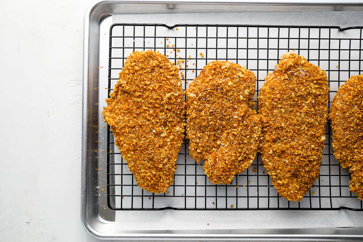 four breaded chicken breasts on a cooling rack.