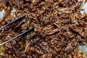 shredded pork carnitas with tongs.