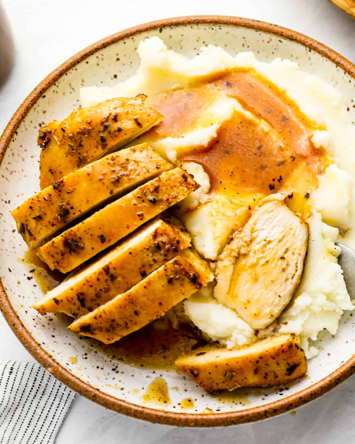 overhead view of a sliced and partially eaten chicken breast on a white plate with mashed potatoes and gravy.