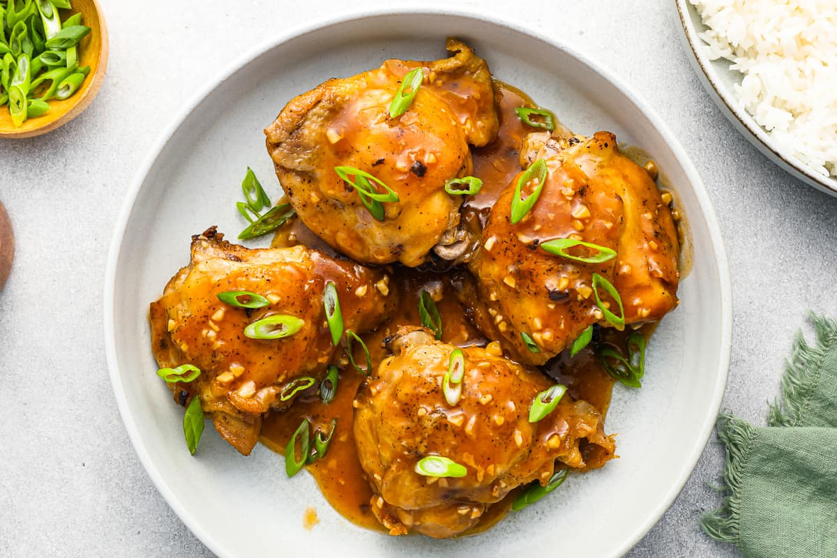 chicken thighs coated in maple BBQ sauce, with rice and green onions on a white plate.