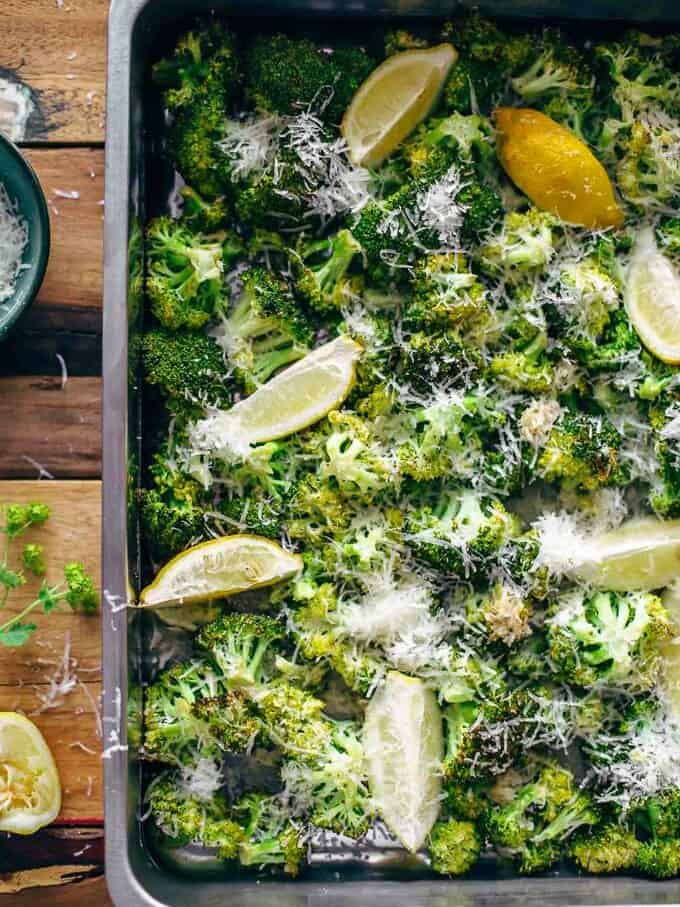 broccoli on a baking sheet with parmesan and lemon wedges