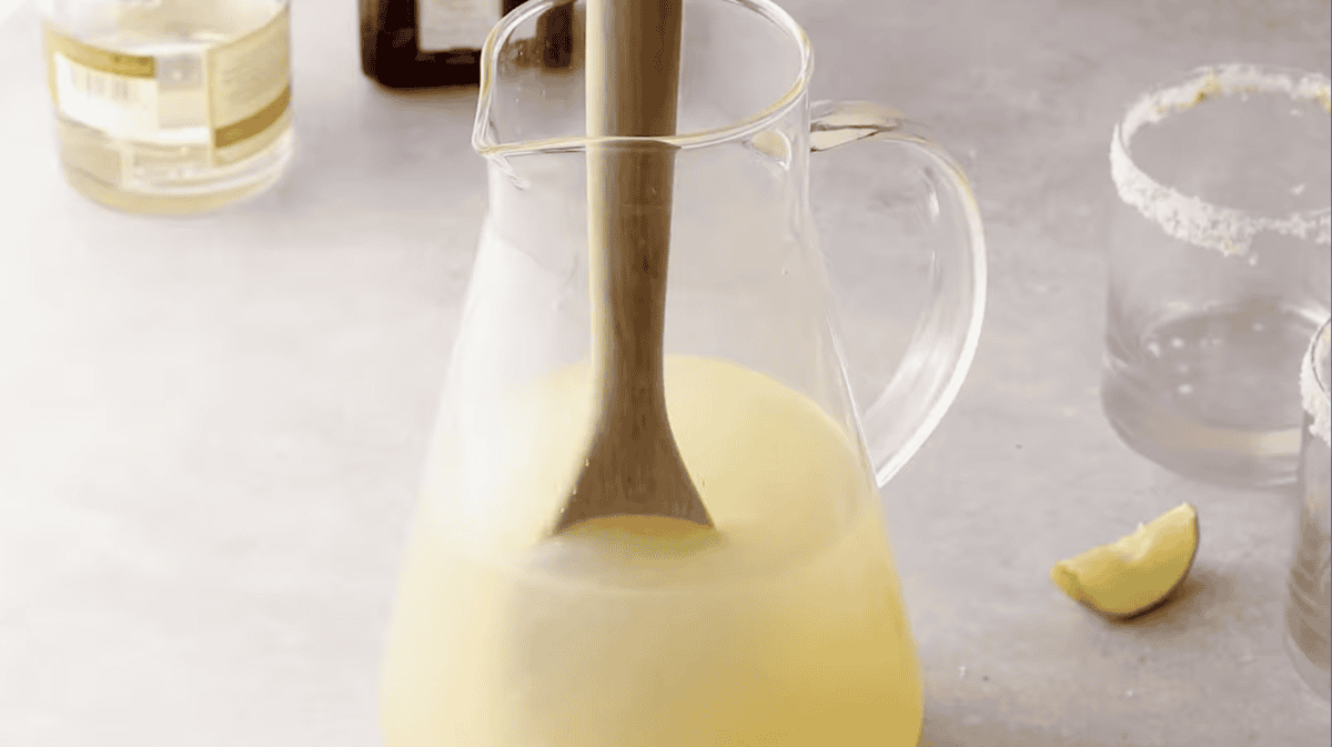 stirring margarita mixture in a pitcher with a wooden spoon.