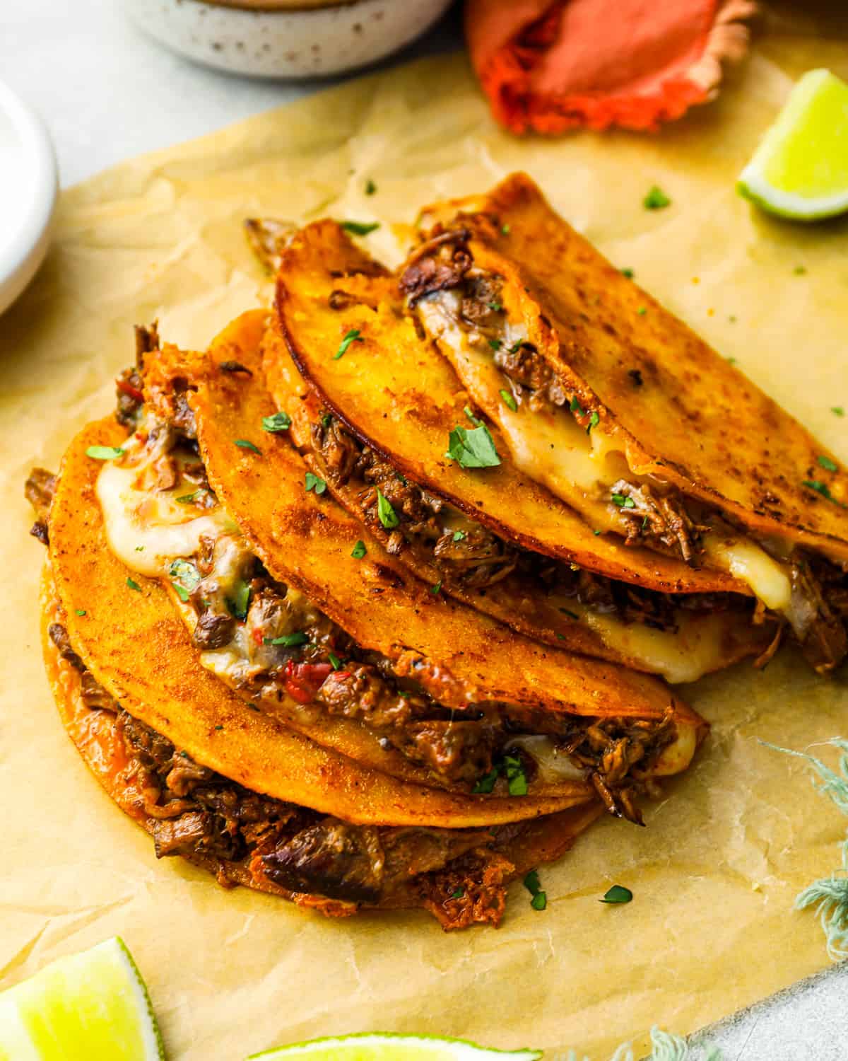 three-quarters view of 4 quesabirria tacos leaning against one another on parchment paper with the filling showing.