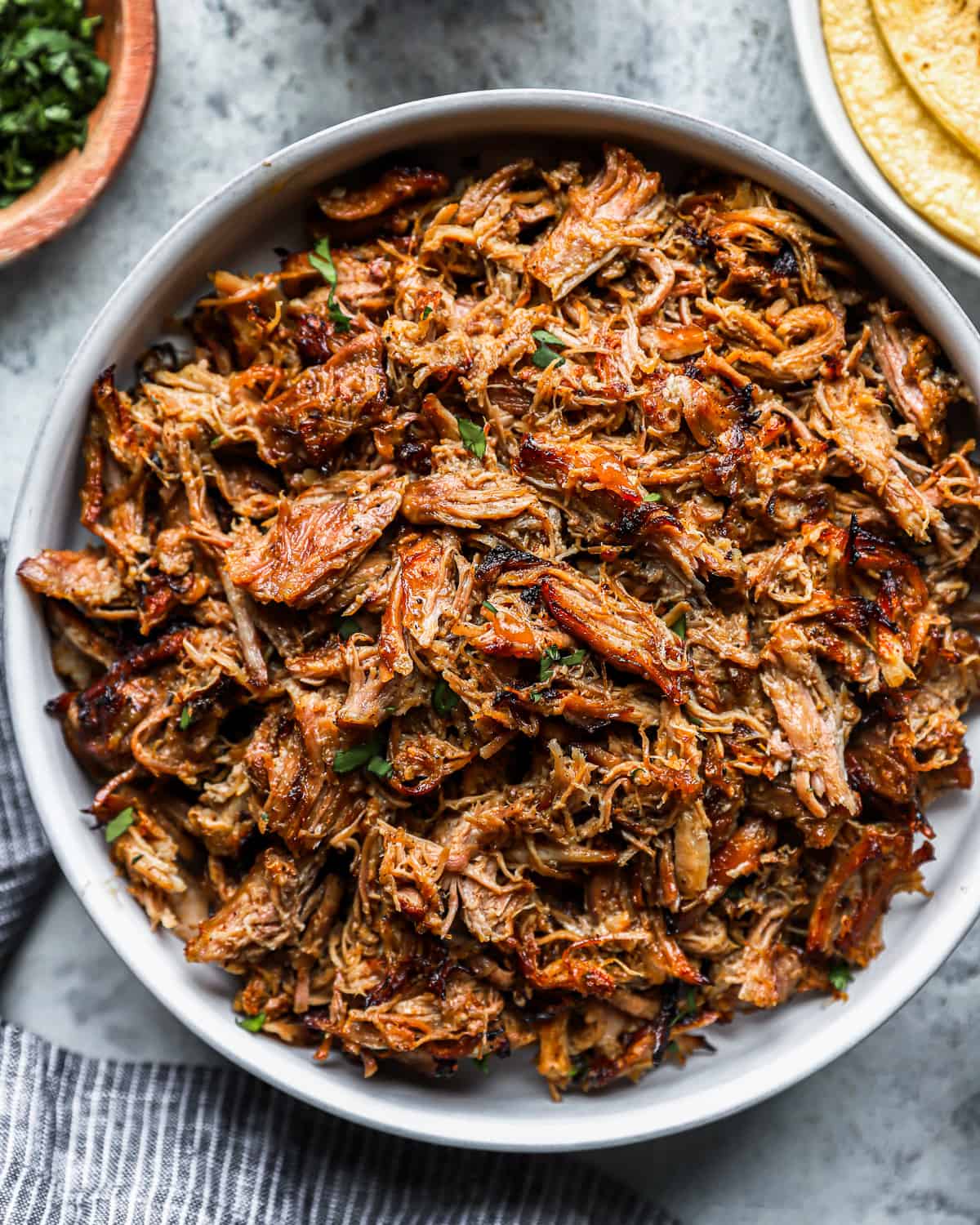 overhead view of pulled pork carnitas meat in a white bowl.