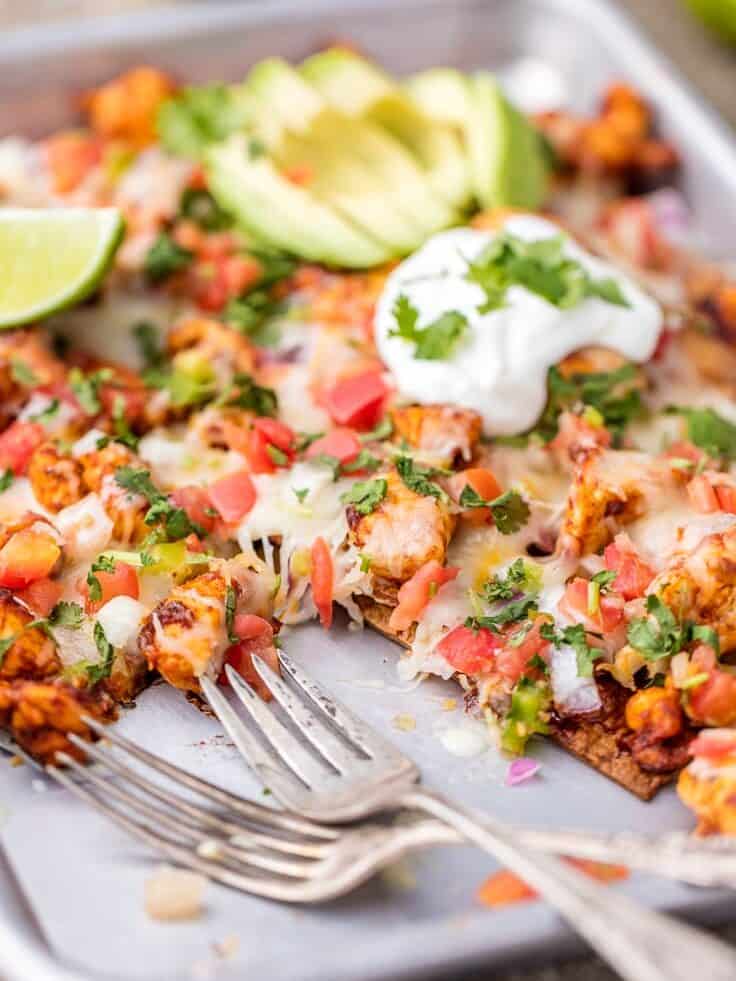 side view of chicken nachos, with two forks set on the sheet pan