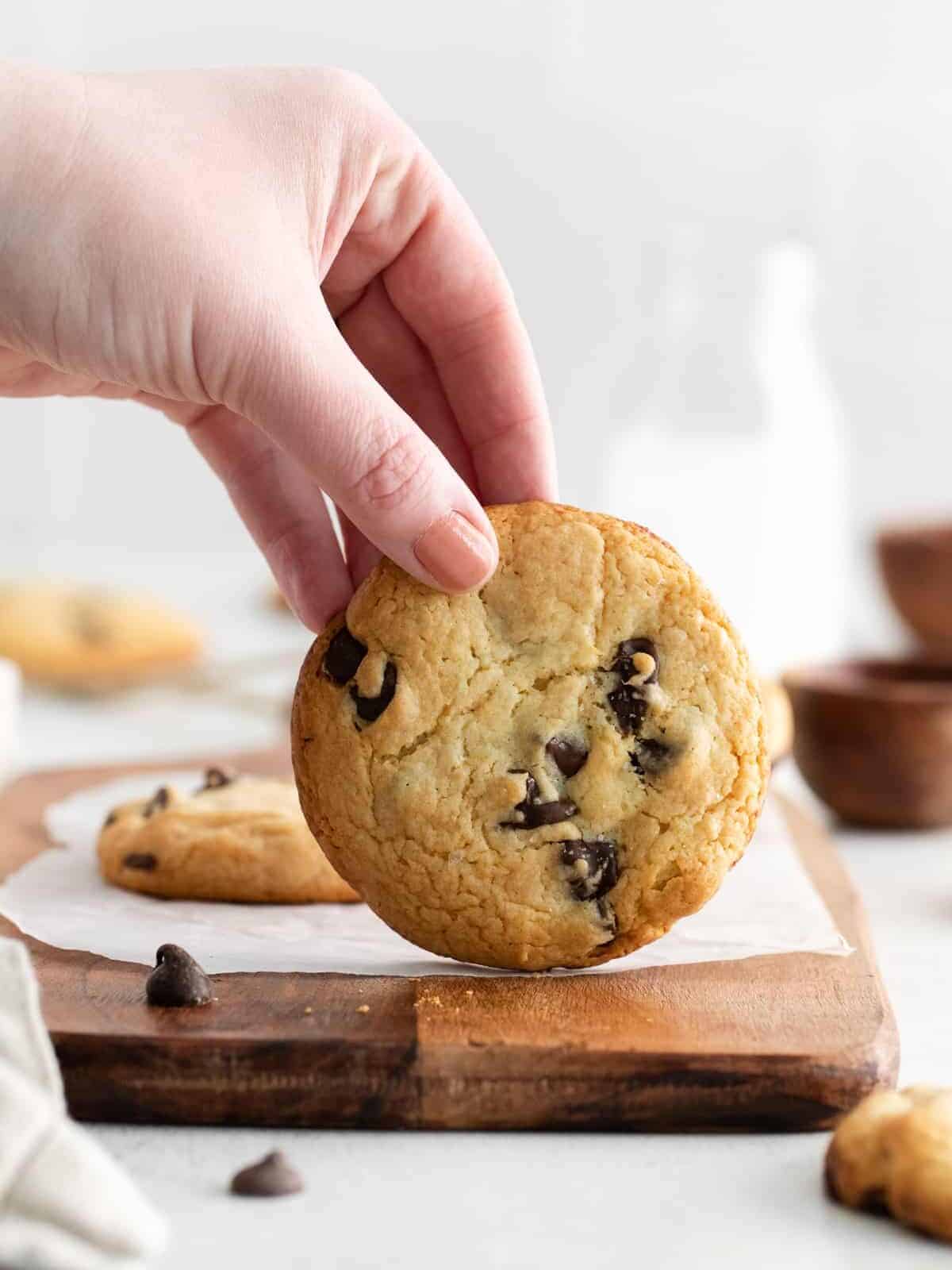 a hand holding a cake mix chocolate chip cookie vertically on a cutting board.