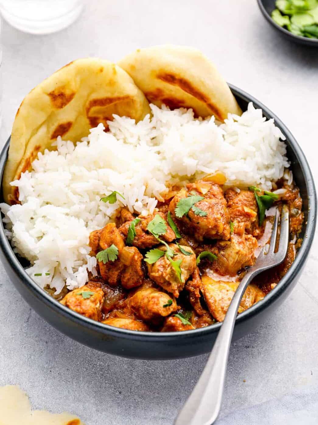 crockpot chicken tikka masala with rice and naan in a black bowl with a fork.