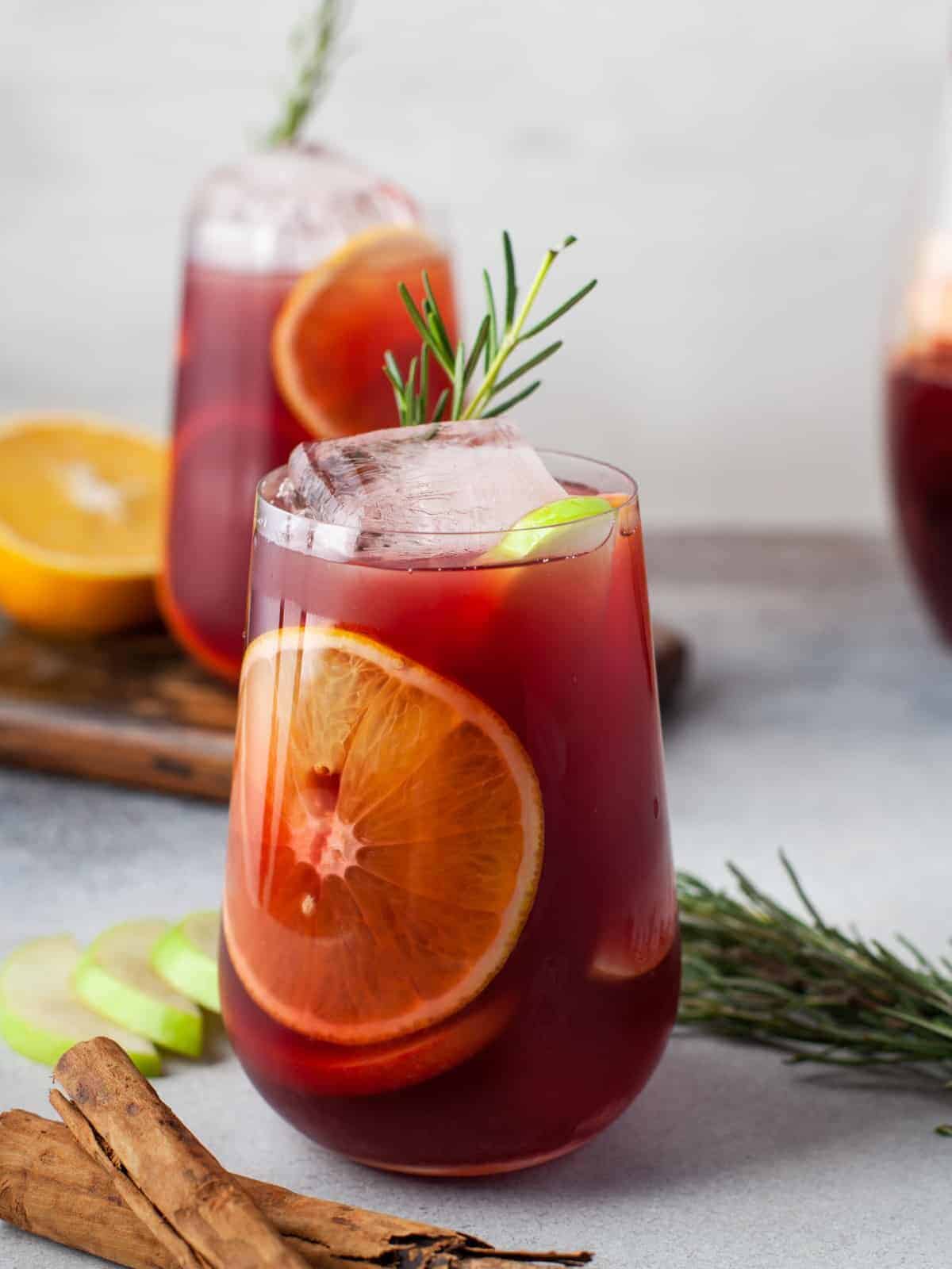 side view of red sangria in a stemless wine glass with ice and rosemary.