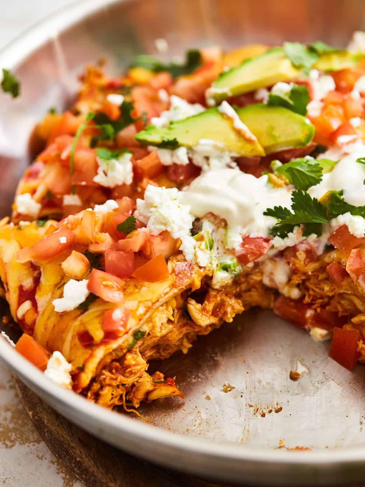 three-quarters view of a chicken enchilada skillet missing one slice in a skillet.