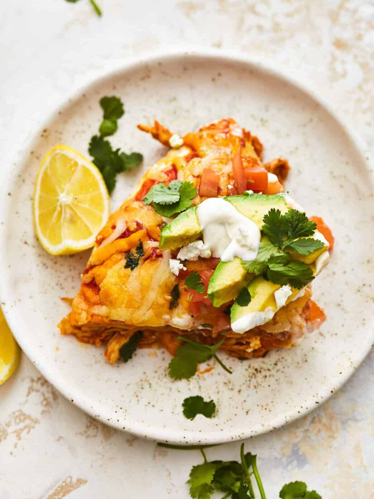 overhead view of a slice of chicken enchilada skillet on a white plate with a lemon.