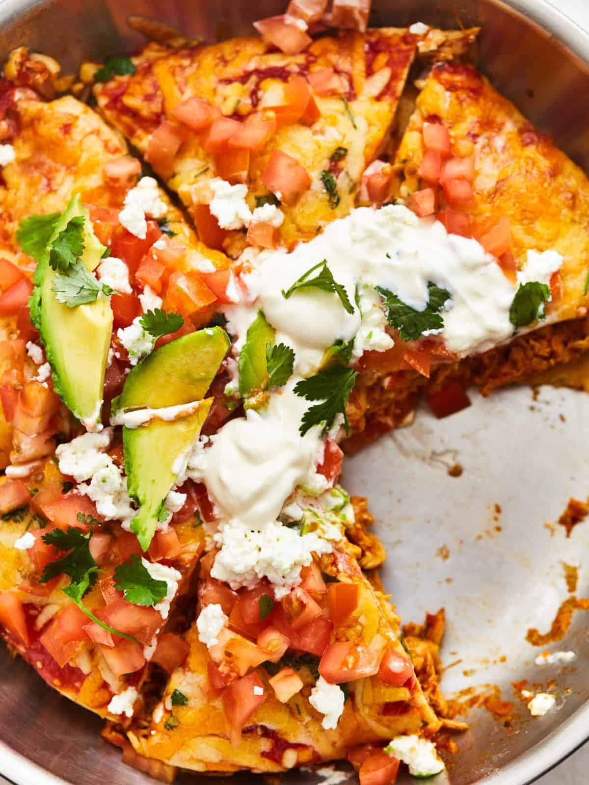 overhead view of a sliced chicken enchilada skillet in a skillet missing a slice.