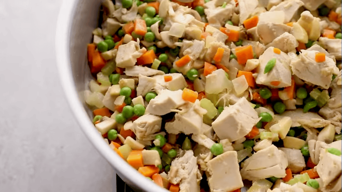 cubed chicken, peas, and mushrooms added to sautéed veggies in a pan.