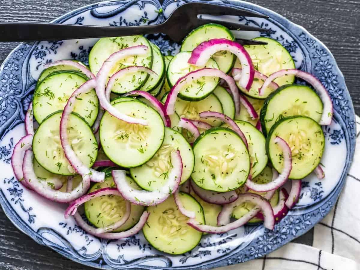 overhead view of cucumber salad with red onions and vinegar dressing, on a white and blue serving plater