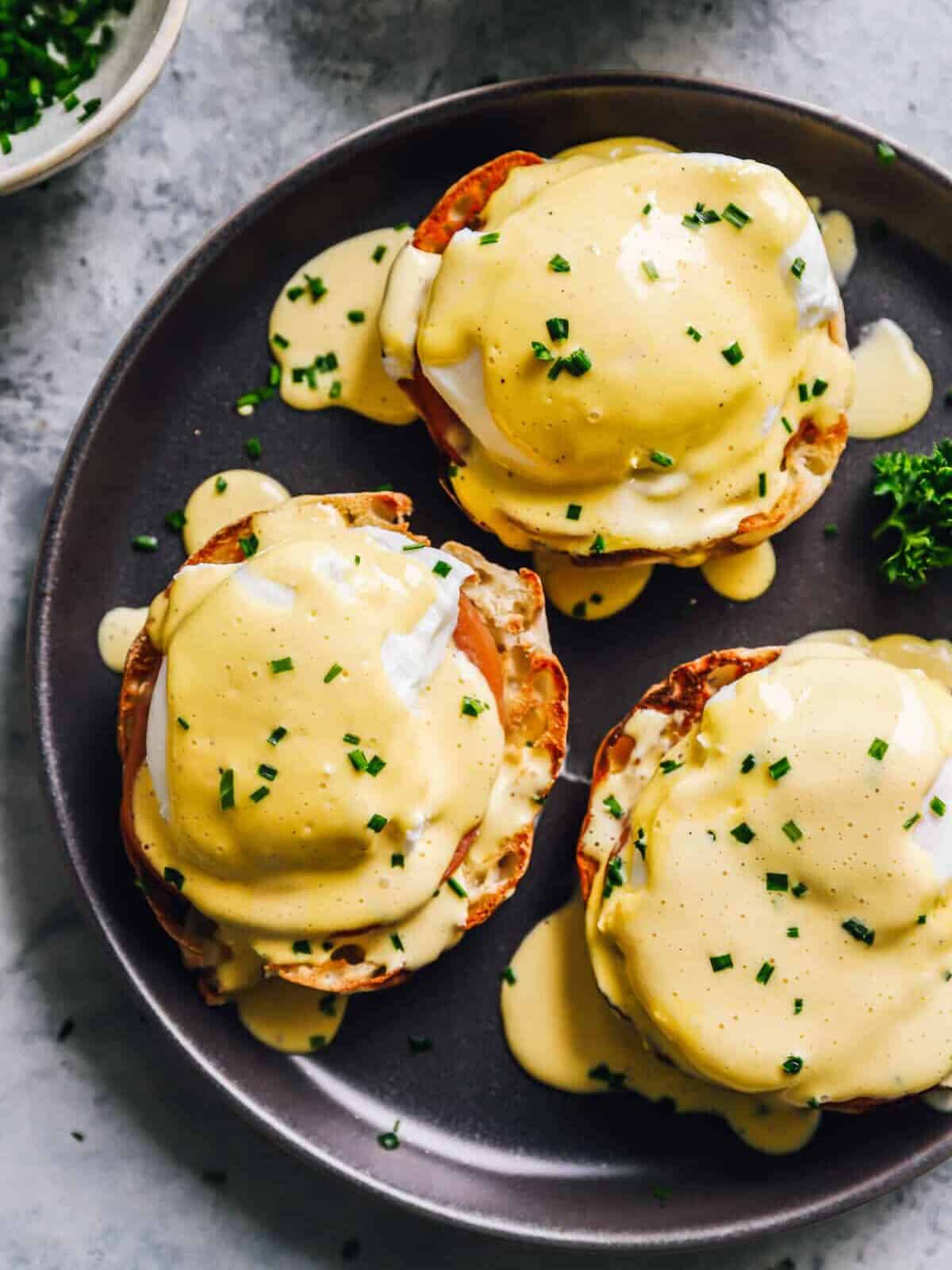 3 eggs benedict on a black plate.