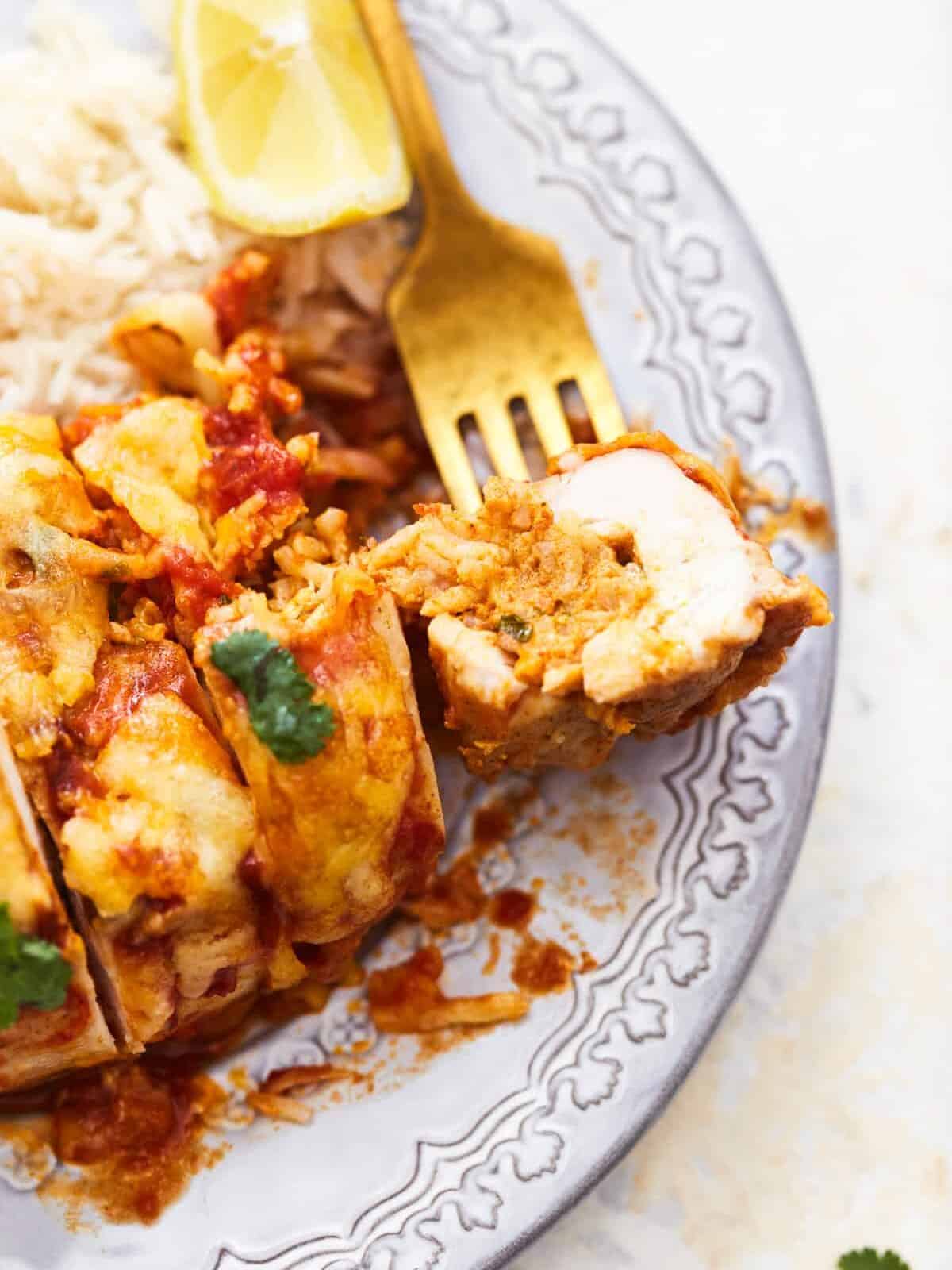 partial three-quarters view of a cut enchilada stuffed chicken breast on a white plate with a fork stabbing a bite.