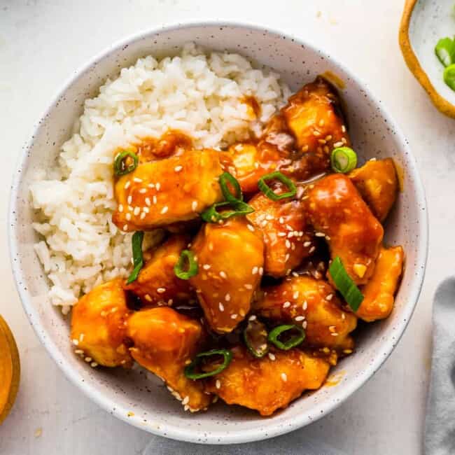 a bowl of asian chicken with rice and sesame seeds.