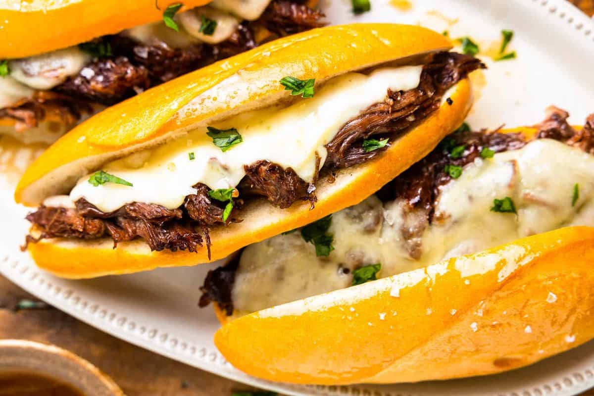 overhead view of 3 french dip sandwiches on a white oval serving tray with au jus.