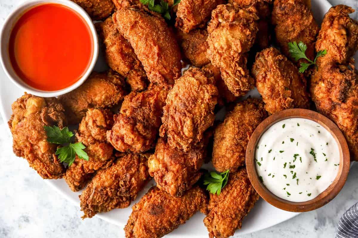 partial overhead view of fried chicken wings on a white platter with buffalo sauce and ranch.