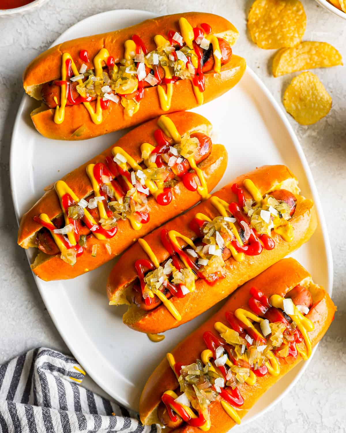 overhead view of 4 topped hot dogs on a white plate.