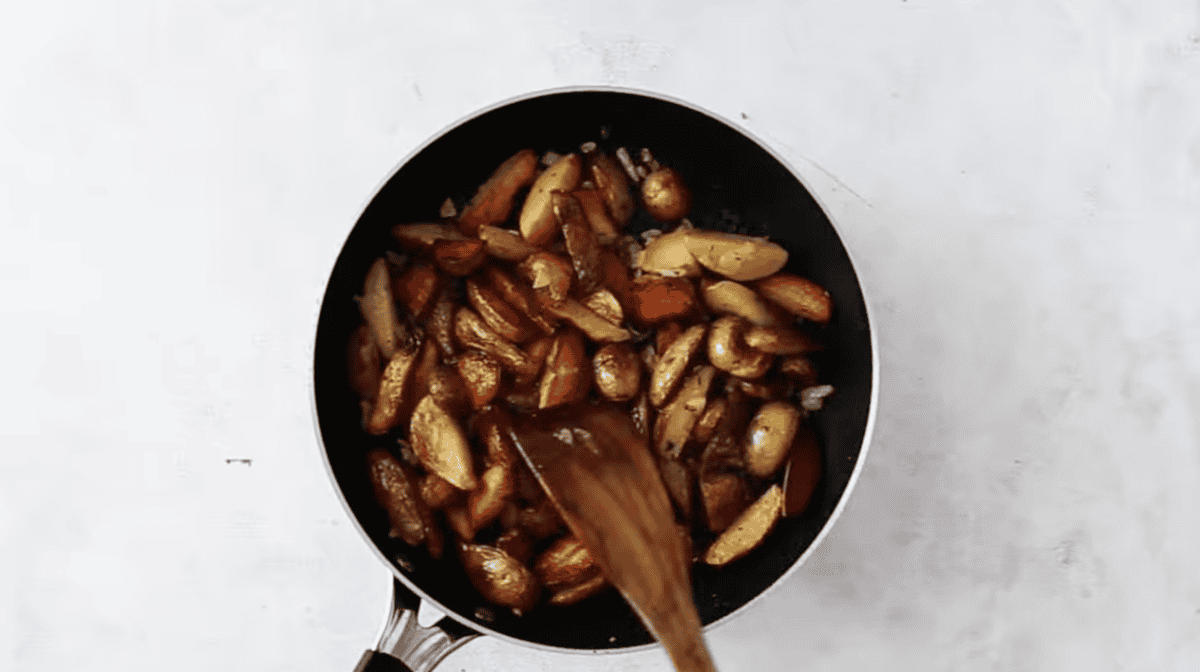 seasoned home fries in a pan with a wooden spatula.