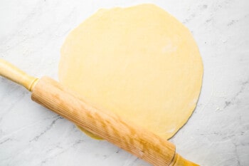 a wooden rolling pin and dough on a marble surface.