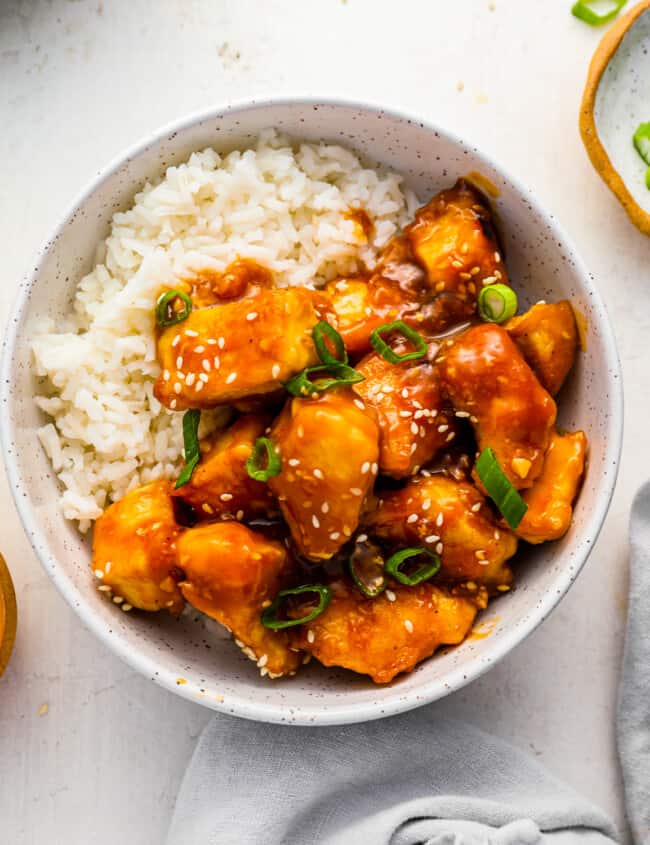 a bowl of asian chicken with rice and sesame seeds.