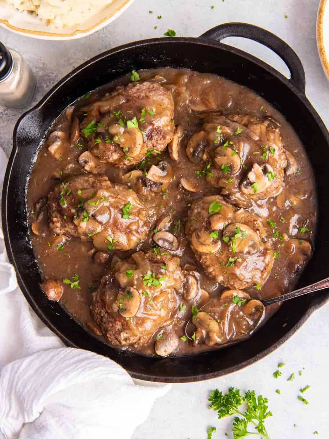 overhead view of 5 salisbury steaks in a cast iron pan.