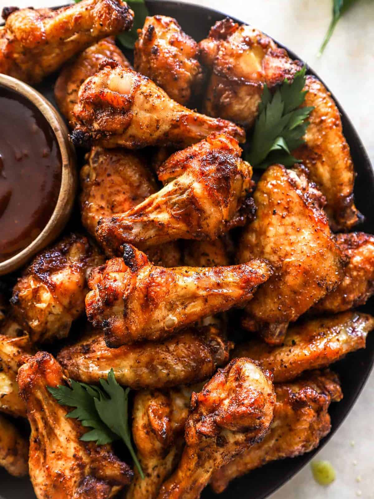 overhead view of smoked chicken wings on a black serving plate with barbecue sauce.