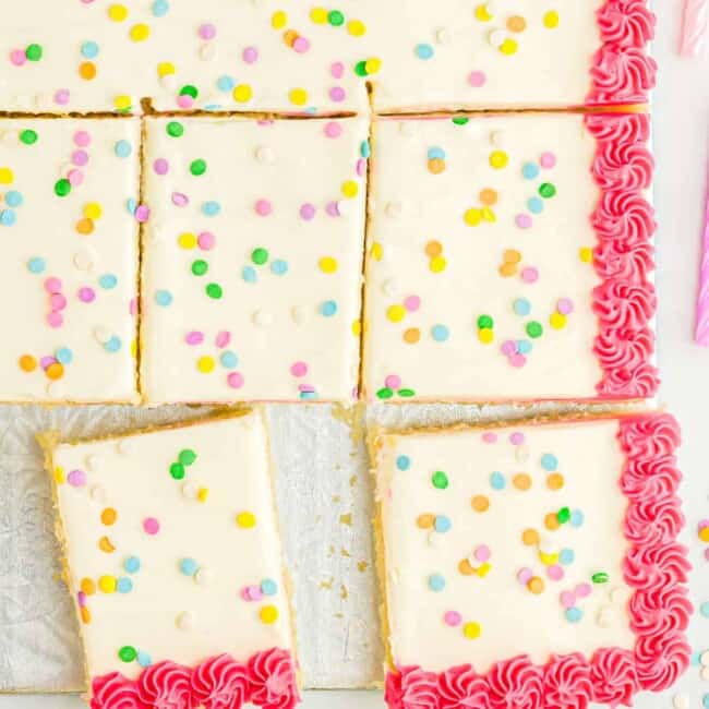 close up overhead view of a partially sliced vanilla cake decorated with white icing with a pink border and sprinkles.