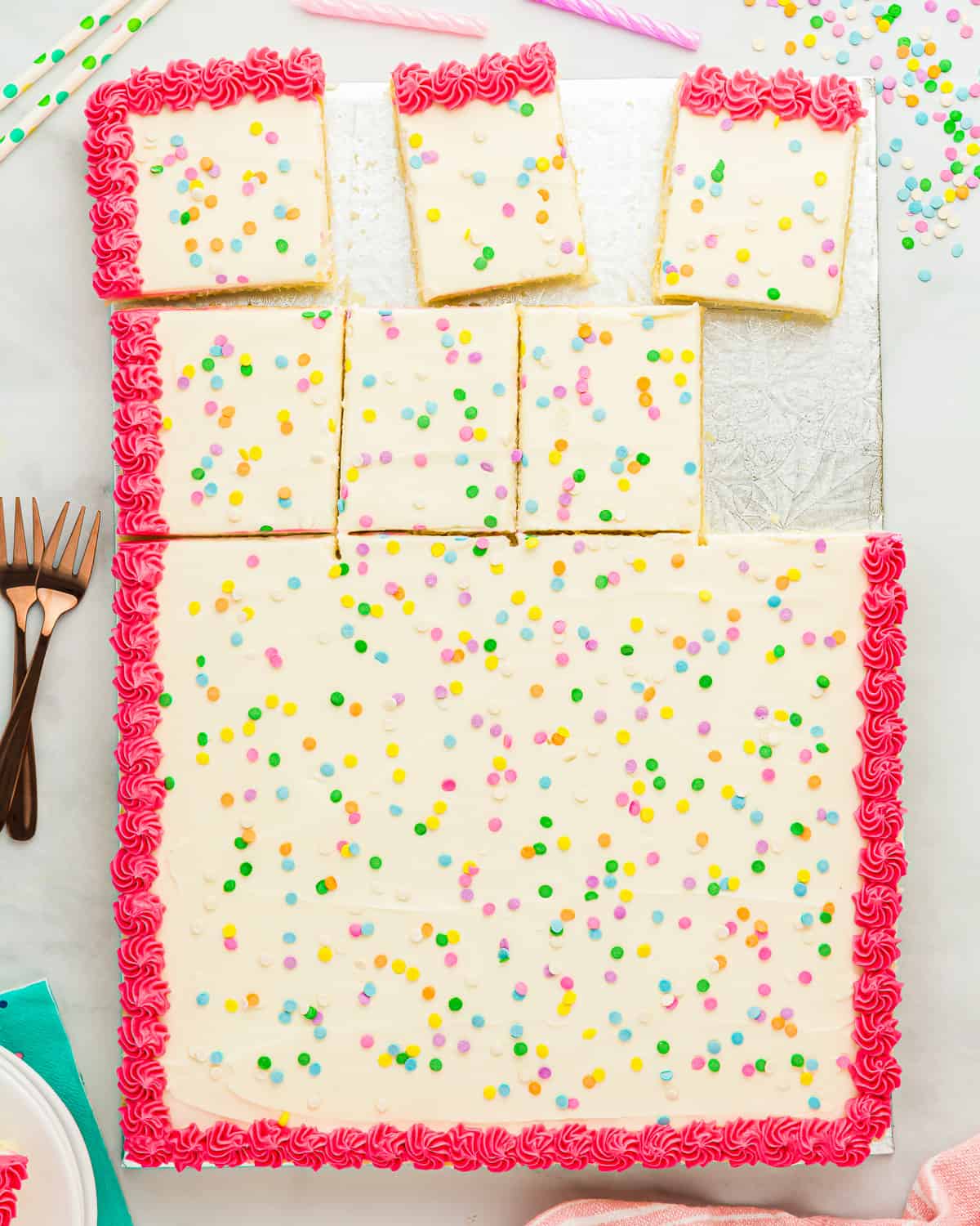 overhead view of a partially sliced vanilla cake decorated with white icing, with a pink border and colorful sprinkles.