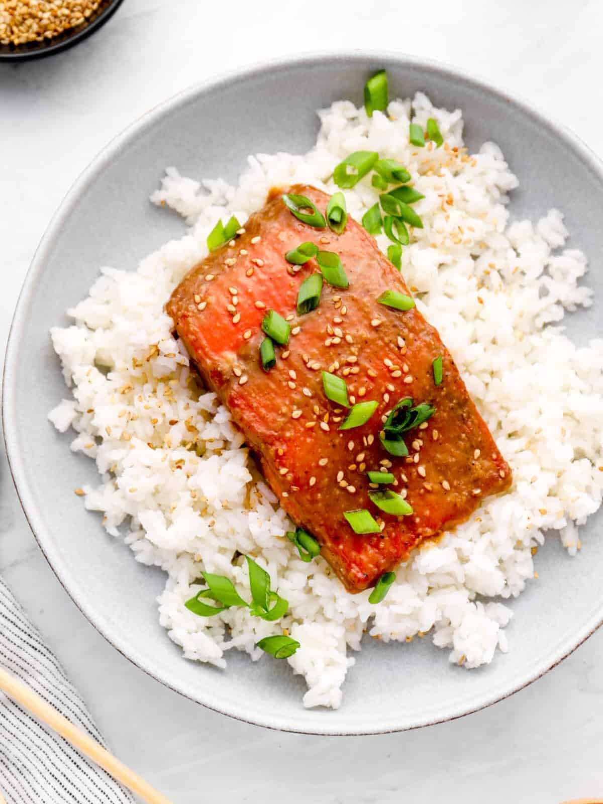 overhead view of miso glazed salmon on a bed of white rice on a white plate.