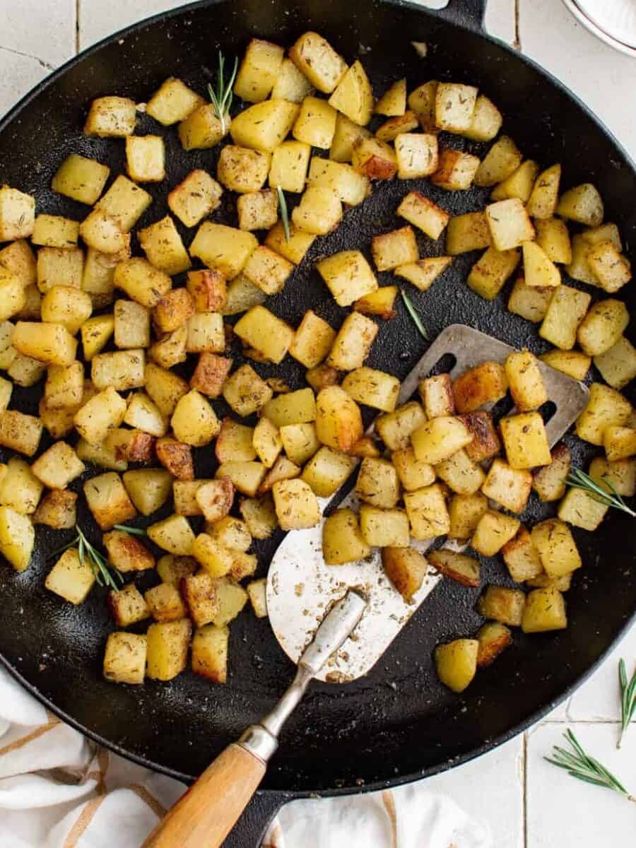 overhead view of breakfast potatoes in a cast iron skillet with a spatula.