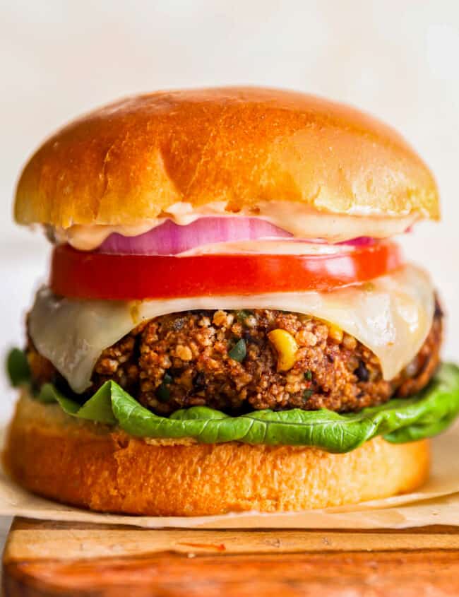 a burger with lettuce, tomato and onion on a wooden cutting board.