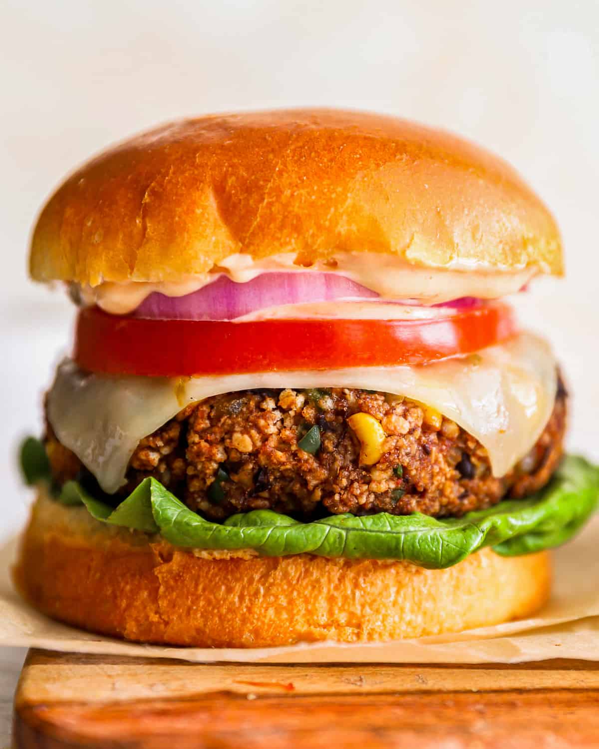 a black bean burger on buns with lettuce, tomato and onion; on a wooden cutting board.