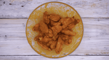 chicken wings tossed in buffalo sauce in a glass bowl.