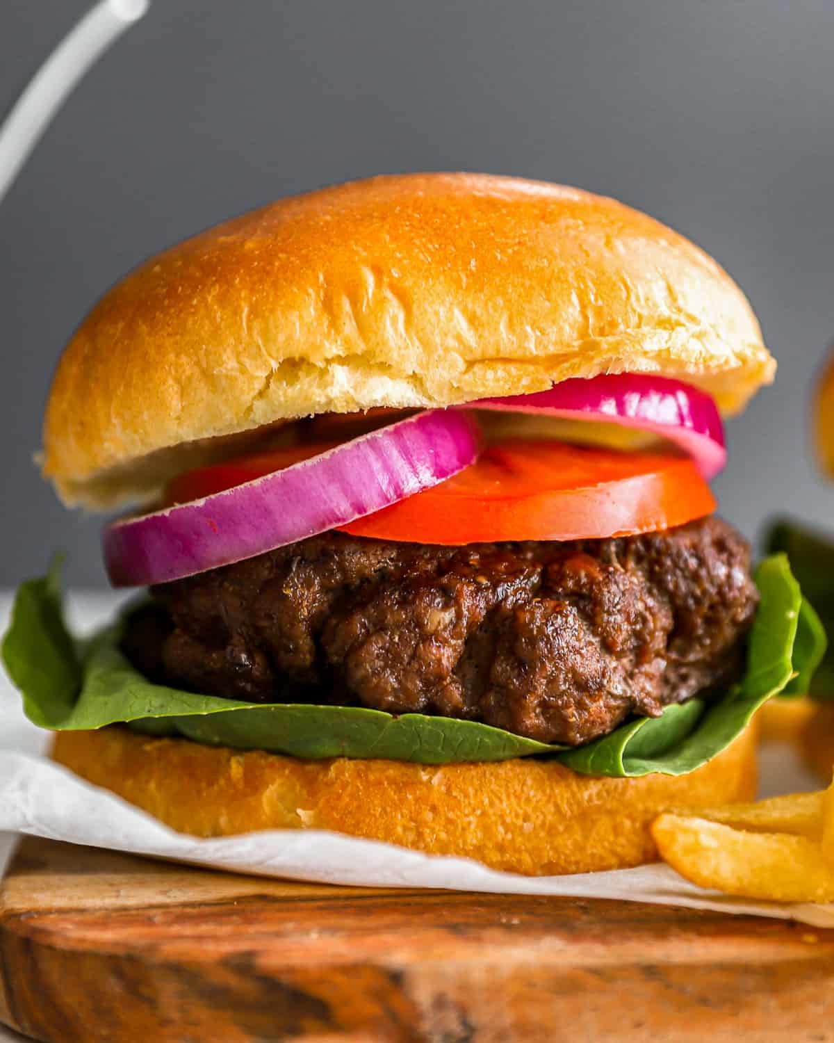 close up on a hamburger, made with a seasoned burger patty, tomatoes, red onions, and lettuce.