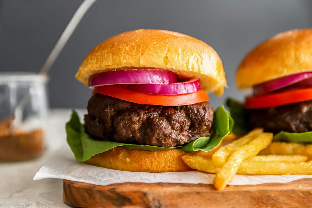 two beef burgers on a wooden cutting board.