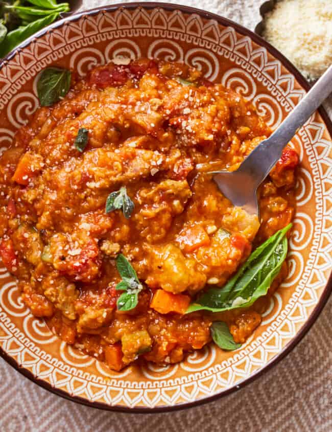 overhead view of a serving of sausage lentil soup in a patterned bowl with a spoon.