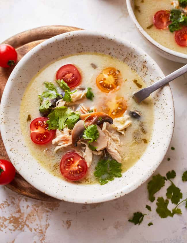 overhead view of a serving of Thai coconut chicken soup in a white bowl with a spoon.